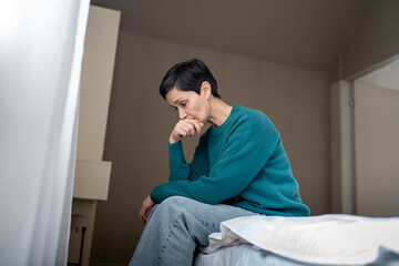 Depressed subdued mature woman grieving in sorrow sitting on bed head down. Agoraphobia, social...