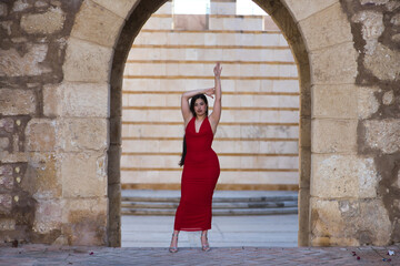 Young, pretty, brunette woman in pretty red party dress and heels, posing looking at camera with...