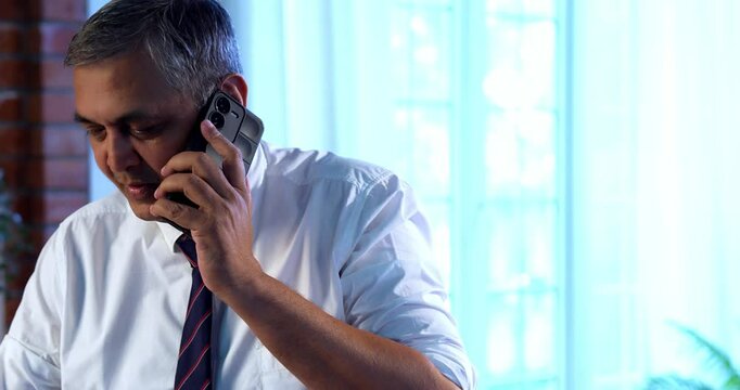 Indian executive working on computer while attending phone call at desk in modern office, Asian corporate professional multitasking with focus and communication skills in contemporary workplace setup