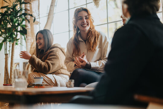 Group of friends sharing laughter and conversation in a cozy cafe with natural sunlight.