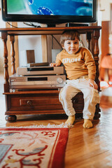 A young child wearing comfortable apparel poses indoors by a vintage TV and entertainment center,...