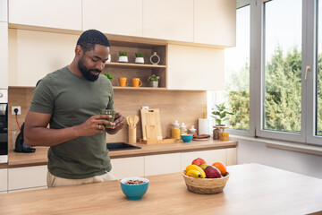 Morning routine, simple living. One man standing in the kitchen, drinking coffee, eating healthy...
