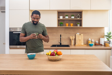 Morning routine, simple living. One man standing in the kitchen, drinking coffee, eating healthy...