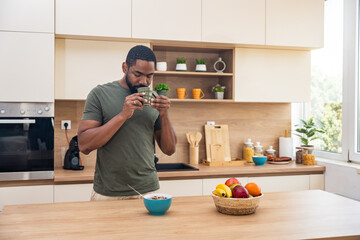 Morning routine, simple living. One man standing in the kitchen, drinking coffee, eating healthy...