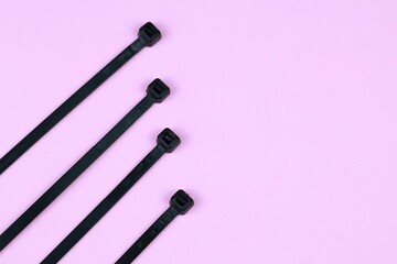 Black Cable Tie or flexible self locking plastic zip isolated on pink background. Come in different sizes, lenghts, material and colors.