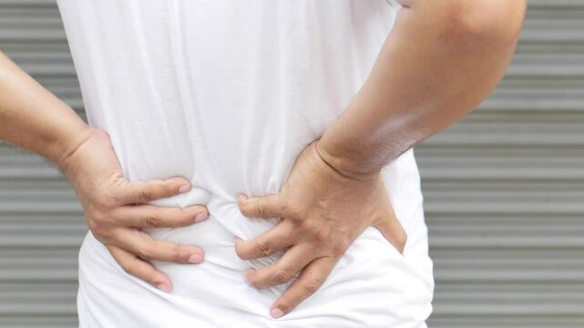Middle-aged Asian man suffering from lower back pain, herniated disc, spinal dislocation, gout arthritis, osteoporosis, hand closeup shot