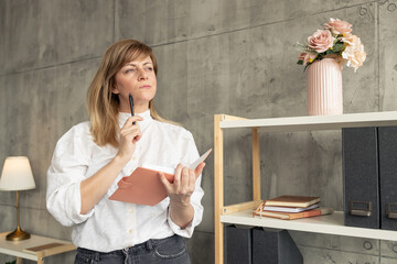 Businesswoman holding notebook and pen, thinking about business strategy in office