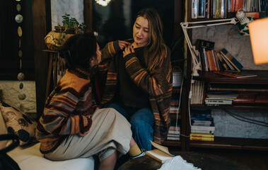 Two female friends having a pleasant conversation in a warmly lit living room with books and...