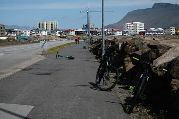 Bicycles and scooters parked near a pathway in Akranes under mountain view