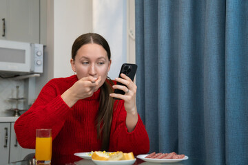 Young woman in a vibrant red sweater enjoying a nutritious meal at the kitchen table while engaging...