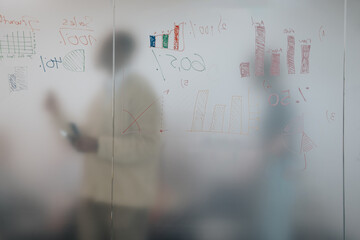 Colleagues engage in creative brainstorming, analyzing charts and graphs on a frosted glass board...