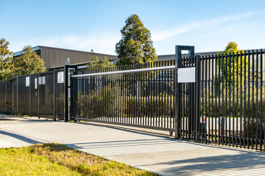 Modern black steel security gate outside a contemporary public facility or school campus in Australia, featuring vertical bars, sliding mechanism, and mounted signage.