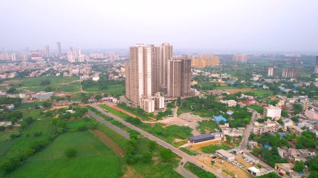 Aerial drone shot flying towards under construction building in the middle of green fields showing the rapid growth of multistory high rise houses and offices