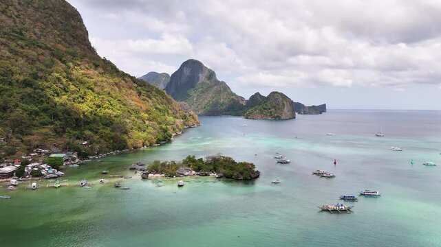 Traditional boats float in Bacuit Bay, surrounded by the dramatic karst limestone formations, tropical foliage of El Nido, a coastal paradise on Palawan Island facing the South China Sea, static shot
