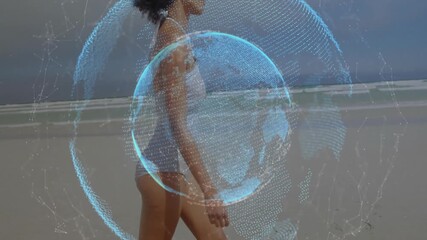 Woman walking on beach activating rotating digital globe showing global technology connectivity - Powered by Adobe