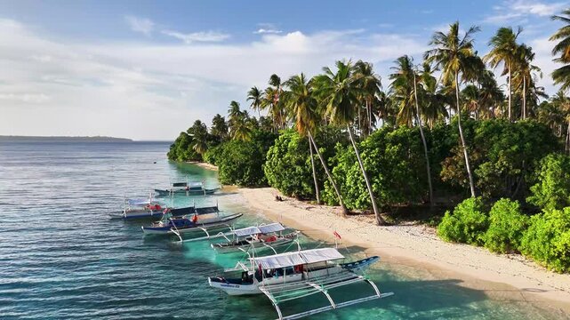 Drone shot of Caxisigan Island&rsquo;s white sand shore lined with tropical trees and outrigger bancas, surrounded by the clear turquoise waters of the Balabac Strait in southern Palawan, Philippines.