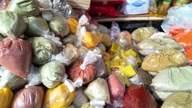 Panning close-up of colorful spices in bags at a Venezuelan market, ending with a handwritten price sign.