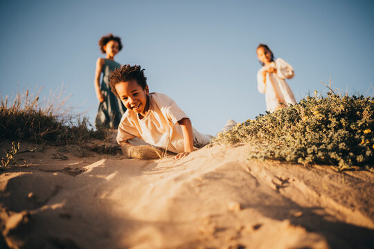 Black boy girl running around sand dunes at beach sunset fun