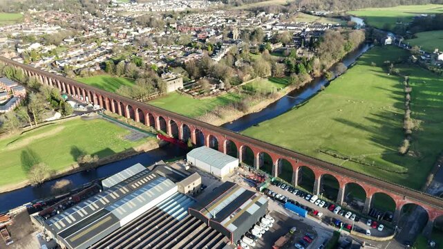 Captivating aerial footage of Conisbrough Viaduct in South Yorkshire, England. Sunlit town, lush fields, and winding river create a tranquil, scenic landscape with no people visible.