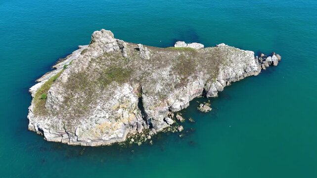 Thatcher Rock in Torquay, showing its rugged cliffs and rocky base surrounded by clear blue sea