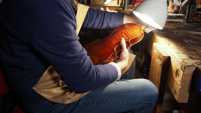 Master artisan gently hand-rubs a varnished violin using traditional French polishing technique, inspecting its chatoyancy under direct light for tonal and visual refinement, real time.
