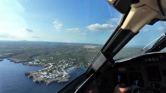 A pilot’s perspective from a jet airplane cockpit in a real time approach to coastal Manorca Island airport, with a view of the runway ahead and the hand of the pilot grasping flight controls