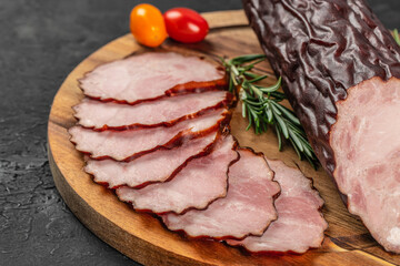 Slices of dry-cured smoked meat with a dark spiced edge are elegantly arranged on a wooden board, garnished with rosemary and cherry tomatoes for a rustic gourmet presentation