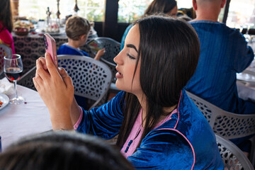 In a lively gathering, a young Arab woman with dark hair dressed in a blue outfit attentively uses...