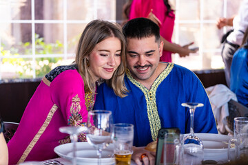 A smiling Caucasian couple gets ready to take a selfie at an Arab cultural celebration, surrounded...