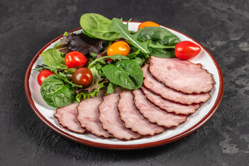 A plate of thinly sliced smoked meat is served alongside a colorful mix of leafy greens and cherry tomatoes, creating a fresh and appetizing presentation