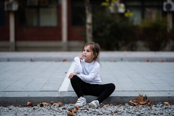 Pensive little girl sitting on curb thinking and daydreaming