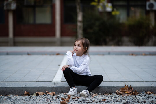 Pensive little girl sitting on curb thinking and daydreaming