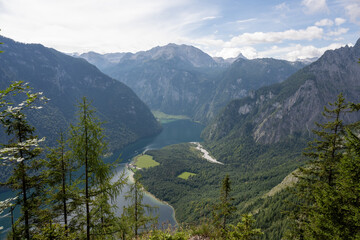 View from above of Koenigsee in Bavaria, Germany the weather is sunny with haze, the sky is blue The lake is mountainous and there are green mountains around it.