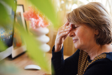 An elderly woman in casual clothes is tired of working at a computer.