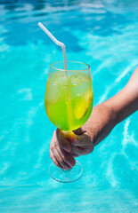 A delicious green cocktail in a glass in a male hand in the pool. A man holds a cup of chilled...
