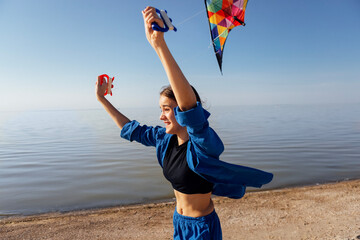 A teenager in casual clothes flies a kite on the beach. The girl laughs and runs along the sandy...