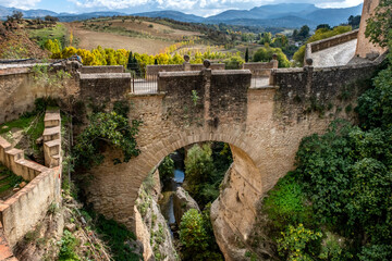 Obraz premium The Puente Viejo, Old Bridge, beside the ancient city walls of Ronda, southern Spain, with a scenic view of the surrounding Serranía de Ronda mountain range of Andalucia.