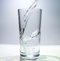 A stream of water flows into a transparent glass The water swirls at the bottom of the glass.