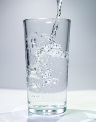 A stream of water flows into a transparent glass The water swirls at the bottom of the glass.