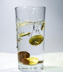 Several coins fall into a glass of clear water Air bubbles are visible in the water