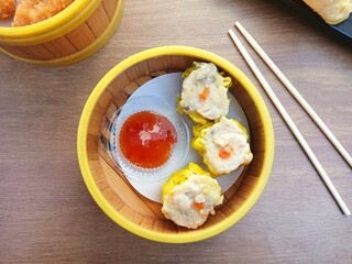 Delicious dim sum and spicy Thai sauce served in bamboo klakat, with bamboo chopsticks on wooden table.