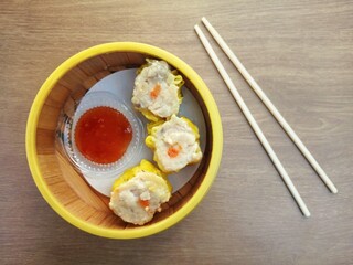Delicious dim sum and spicy Thai sauce served in bamboo klakat, with bamboo chopsticks on wooden table.