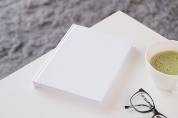 blank book mockup on white coffee table with green matcha tea near window