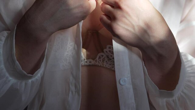 Woman unbuttoning white shirt revealing belly piercing and lace bra