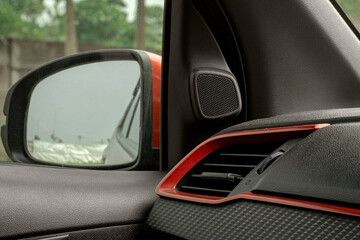 Close-up of a modern car interior, featuring the side mirror, tweeter speaker, and air vent with red accents and a carbon fiber texture.