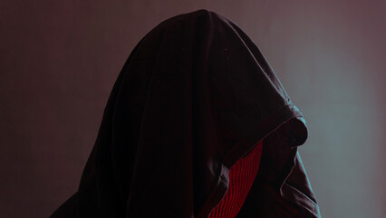 Hooded and masked figure under red ambient light against dark backdrop, ninja-style mystery...