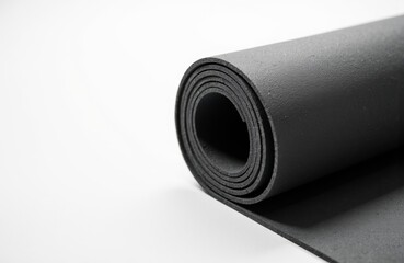 Black yoga mat rolled up on a white surface with space for text or branding