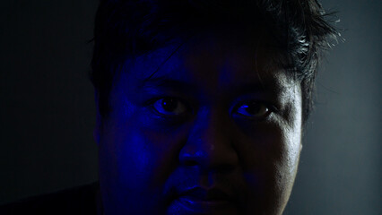 Close-up male face partially lit by blue ambient light against black background, mysterious and shadowy expression emphasizing suspenseful cinematic mood