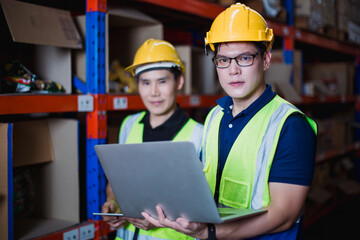 Asian industrial engineers working in warehouse using laptop to monitor inventory and logistics operation for efficient supply chain management. Logistics teamwork concept,
