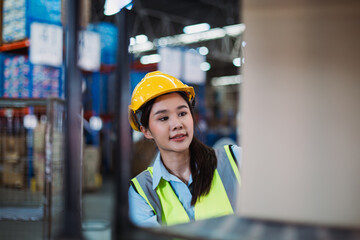 Young Asian woman wearing helmet and reflective vest lifting package in warehouse, highlighting...